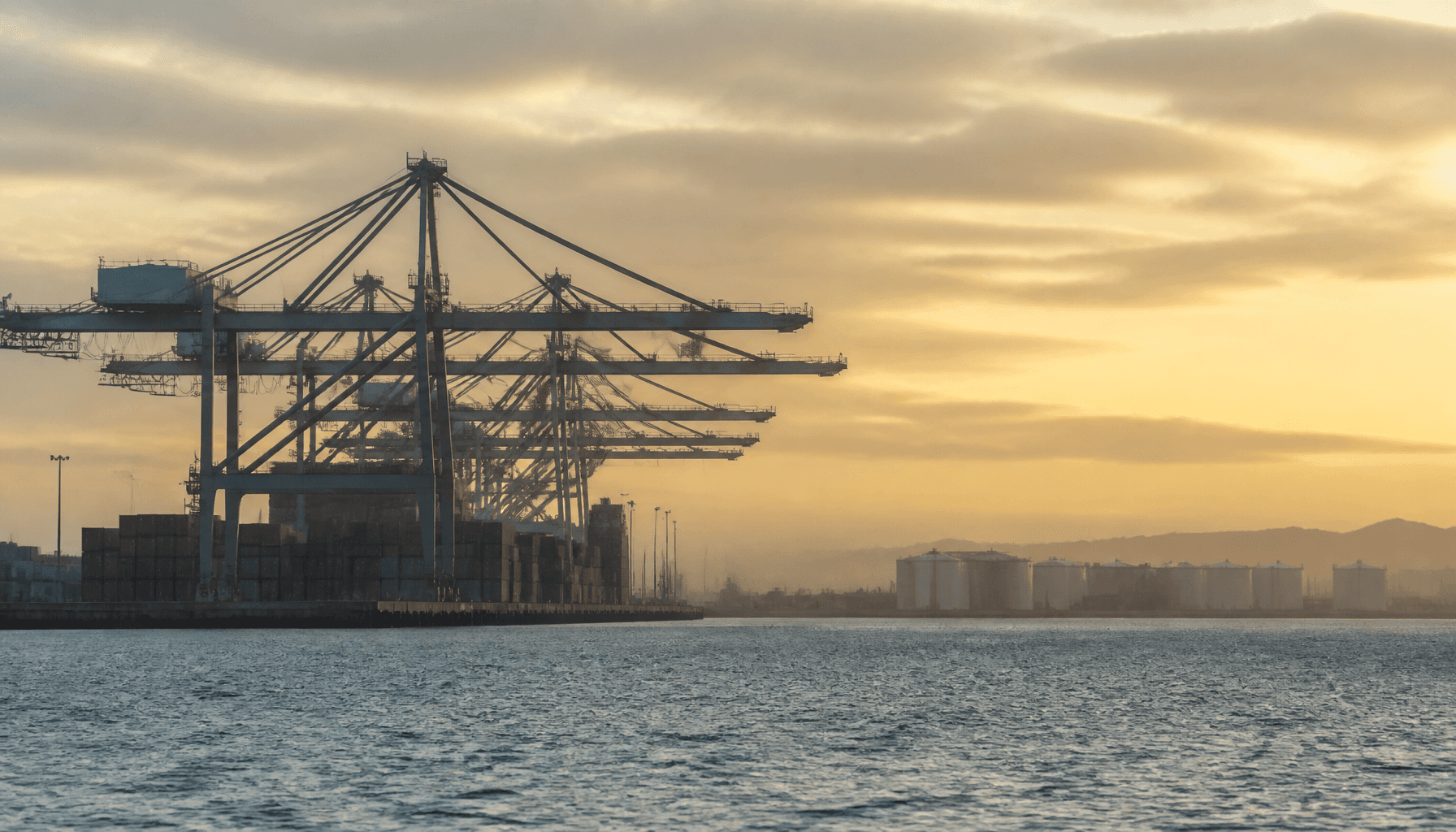 Port of Tauranga container cranes and fuel storage tanks at dawn under hazy amber sky