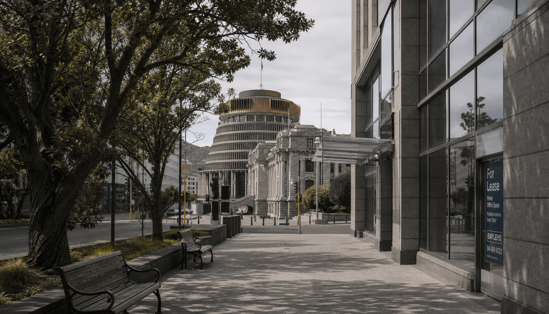 Wellington's Lambton Quay looking toward the Beehive on an overcast morning, a For Lease sign visible in a ground-floor office window