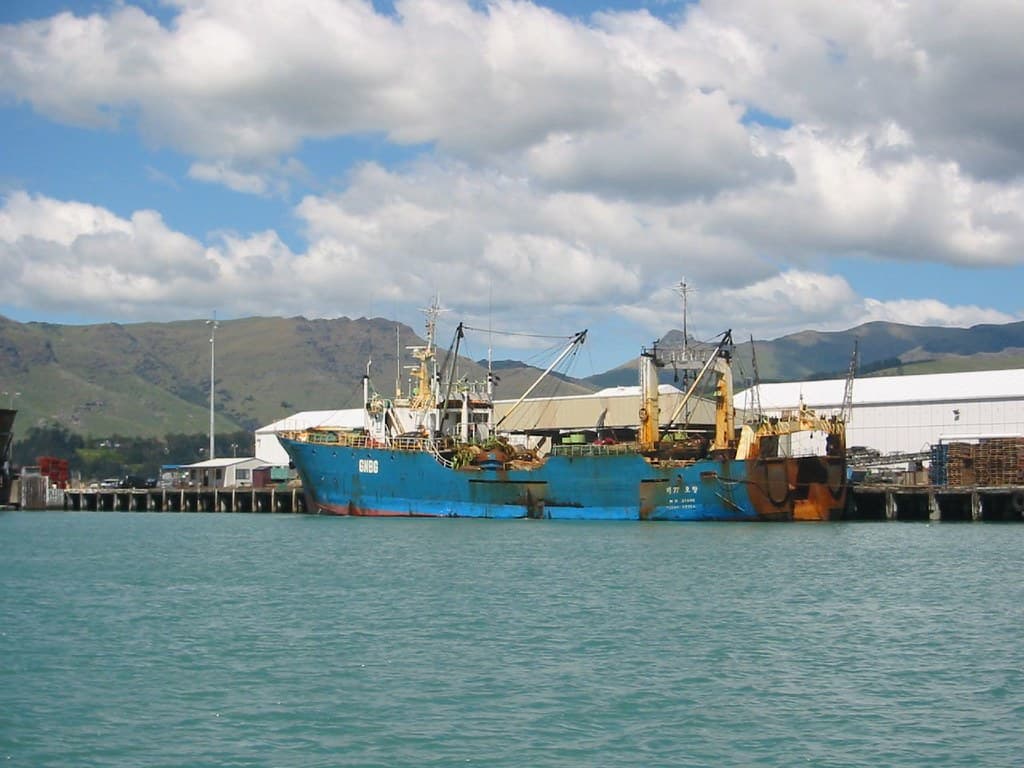 A cargo ship docked at Lyttelton Port, New Zealand, with cranes and containers visible on the wharf