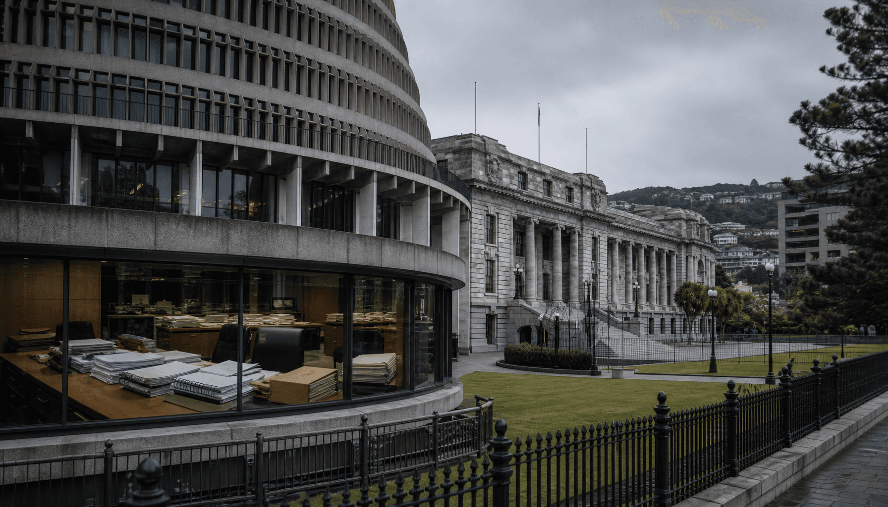 The Beehive and Parliament Buildings in Wellington under grey midday light, with government folders visible on a desk in the foreground